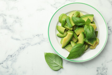 Cut ripe green avocado and basil on white marble table, top view. Space for text