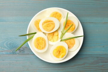 Halves of hard boiled eggs with green onions on blue wooden table, top view