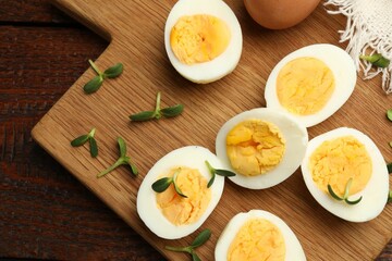 Halves of hard boiled eggs with microgreens on wooden table, top view