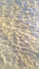 Clear water surface with slight ripples reflecting sunlight creating a background and texture of a calm water environment with sand on the bottom