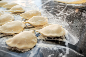 Raw varenyky on a black countertop, top view. The process of making Ukrainian varenyky with cottage cheese.