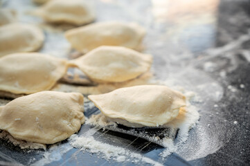 Raw varenyky on a black countertop, top view. The process of making Ukrainian varenyky with cottage cheese.