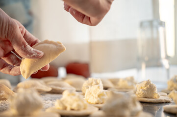 Close-up of a woman's hand holding a raw varenyky with cottage cheese