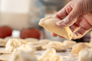 Close-up of a woman's hand holding a raw varenyky with cottage cheese