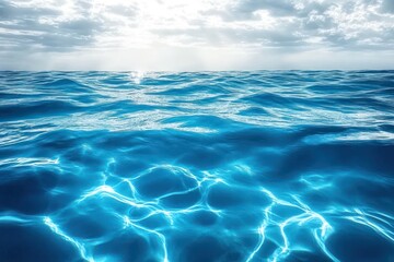 Fototapeta premium Bright sunlight shining through clouds onto vibrant blue ocean waves with sparkling reflections and calm horizon under a partly cloudy sky