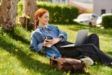 Sun kissed red haired woman enjoying coffee while working on her laptop in a green park