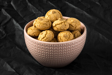 Amaretti cookie in a porcelain bowl on a black background , side view , high-resolution  . Delicious , crunchy biscuits for tea .
