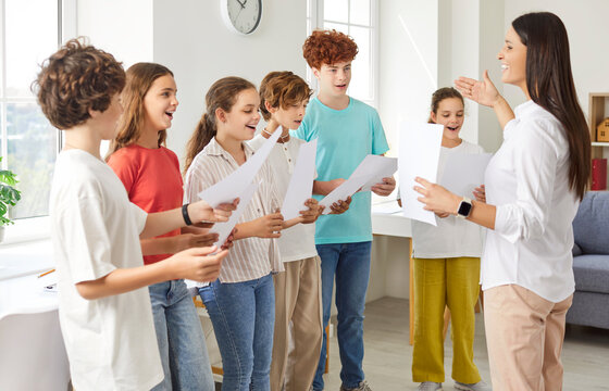Happy school group choir, teaching music class for kids, young active teacher giving vocal lessons, students participate in fun educational musical activities, learn, develop together, enjoy singing