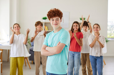 Fototapeta premium Portrait of a happy redhead schoolboy stands in front of classmates in the classroom. Joy of education and learning, highlighting the student enthusiasm for back to school experiences.