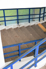 View Looking Down A Concrete Staircase With Slightly Rusty Blue Painted Metal Handrails And Balustrades. Modern Architectural Element With Signs Of Wear.