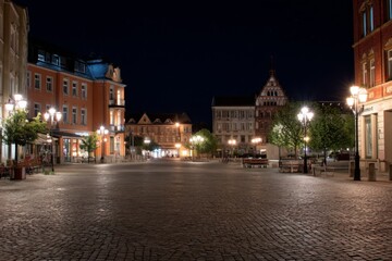Fototapeta premium Inviting Town Square at Night with Cobblestone Paving, Illuminated by Streetlights and Historic Building Facades