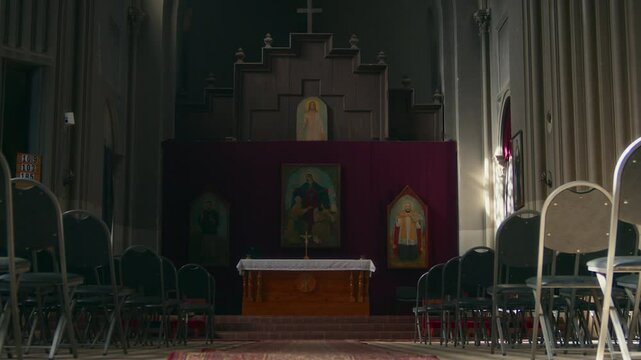 No people zoom in shot of Catholic church interior with altar and icons in background and rows of pews