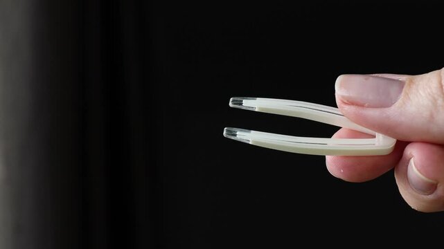 hand holding white contact lens tweezers against dark background with soft lighting, concept of hygiene tools, eye care accessories, safe contact lens handling