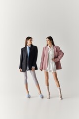 Stylish twin sisters showcase unique fashion in a modern studio setting with playful expressions