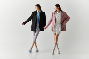 Stylish twin sisters showcase unique fashion in a modern studio setting
