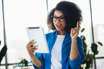 Young businesswoman using digital tablet with enthusiasm, showcasing creativity and professional energy in a modern environment