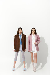 Stylish twin sisters showcase their unique fashion in a minimalist setting