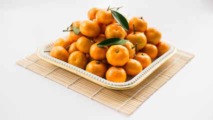 Mandarin oranges arranged in a white square container on top of sushi rolls on a white table