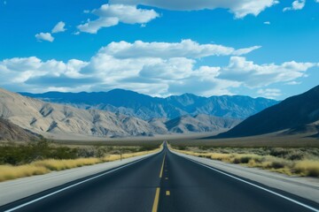 Naklejka premium Long empty highway crossing the scenic landscape of Death Valley National Park under a cloudy blue sky