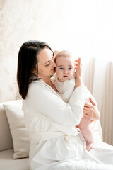 a mother with a baby hugs and kisses, maternal love and care, a mother on maternity leave with a small child at home, a mother with a newborn baby