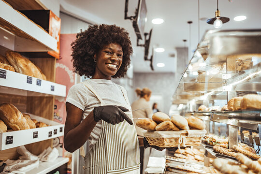 Friendly Baker Smiling While Offering Freshly Baked Bread in Bakery Shop