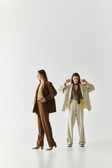 Stylish twin sisters showcasing their fashionable outfits in a minimalist studio setting