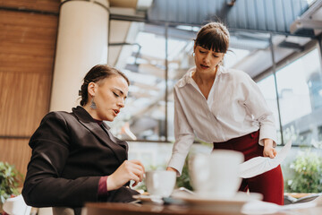 Two women interacting in a professional meeting discussing documents at a cafe.