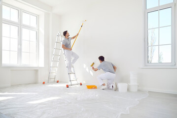 Fototapeta na wymiar Team of male professional painters is working together to paint a wall during a renovation project at a home or office. Teamwork and dedication to improving the space in the construction area.