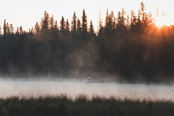 morning hike at sunrise in canada, by a pine tree forest, with misty air and pastel colours, full moon and pale clouds in the sky, by the little quiet pond