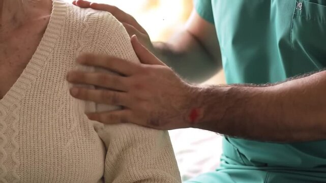 Caring Touch Healthcare Provider Hand on Patient Shoulder Indoor Comfort and Affectionate Support Scene in White Sweater and Green Scrubs