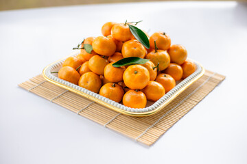 Mandarin oranges arranged in a white square container on top of sushi rolls on a white table