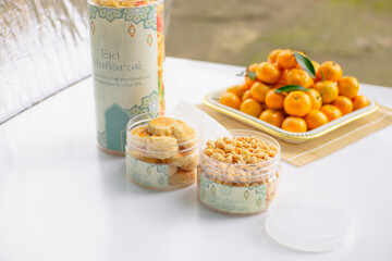 Eid hampers containing dry cakes in jars such as nastar, roasted peanuts without skin, oranges, and sweets on a white background with typical Eid ornaments