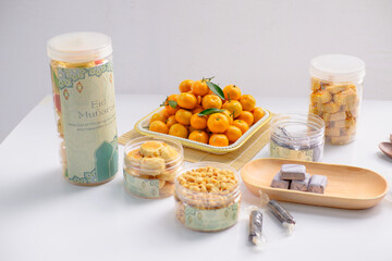 Eid hampers containing dry cakes in jars such as nastar, roasted peanuts without skin, oranges, and sweets on a white background with typical Eid ornaments