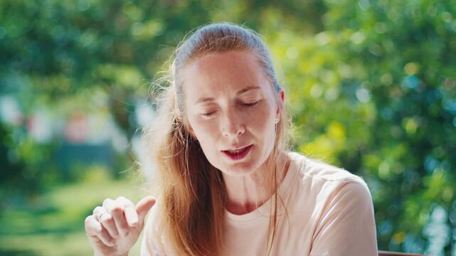 Portrait of the caucasian young adult woman talking during interview with naturally blurred garden on the background