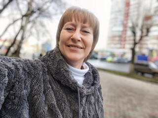 Selfie of a middle-aged woman in a cozy sweater enjoying a sunny day outdoors while blogging about her lifestyle