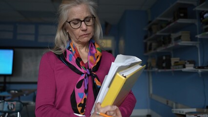 Unhappy middle-aged woman stands in a school classroom. Bright colors accent her outfit as she...