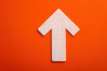Obraz premium A large, textured arrow points upwards against a solid orange background, showcasing a minimalist design. The arrows surface has a subtle grain, adding depth to the composition.