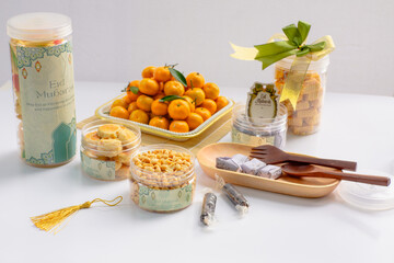 Eid hampers containing dry cakes in jars such as nastar, roasted peanuts without skin, oranges, and sweets on a white background with typical Eid ornaments