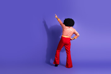 Man in vibrant 70s-inspired outfit pointing upwards on a vibrant purple background embodying retro fashion and disco vibes