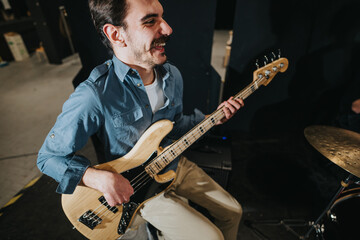 Obraz premium Smiling musician playing bass guitar during a band rehearsal in a studio.