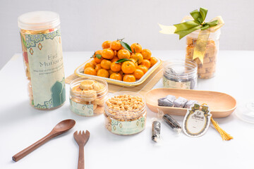 Eid hampers containing dry cakes in jars such as nastar, roasted peanuts without skin, oranges, and sweets on a white background with typical Eid ornaments