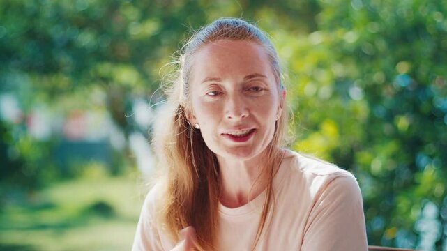 Portrait of the caucasian young adult woman talking during interview with naturally blurred garden on the background