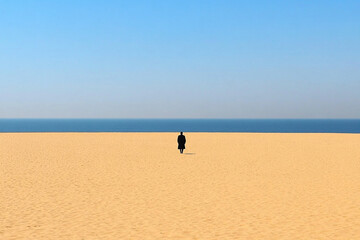 Lonely beach with a solitary figure walking on untouched sand under a clear blue sky