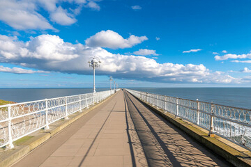 Obraz premium Deserted pier extending over calm sea under bright blue sky with scattered clouds
