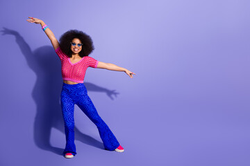 Colorful young woman in retro style fashion posing against a purple background, expressing joy and...