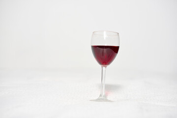 Elegant glass of red wine centered on white surface. Simple, minimalistic background enhances deep red hue, creating visual focus. Soft lighting adds sophistication