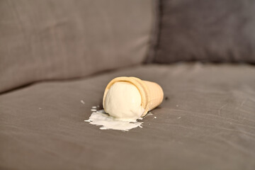 Vanilla ice cream cone lies on grey fabric, melting gradually. Soft lighting creates casual and...