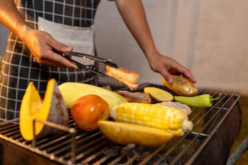 A man enjoys a summer barbecue outdoors, grilling meat and vegetables over open flames, surrounded by friends, smoke, drinks, and weekend freedom.

