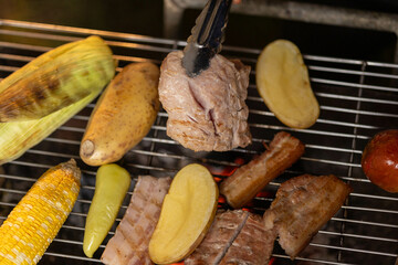 A glowing barbecue grill sizzles with assorted meats and vegetables, flames and smoke rising in the dark, capturing the essence of a summer cookout.
