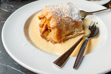 Apple strudel with vanilla custard sauce on a plate with two sets of utensils